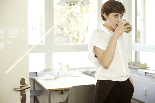 Woman drinking glass of green smoothie in an office