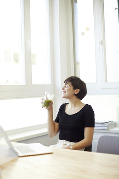 Happy woman drinking green smoothie in the office