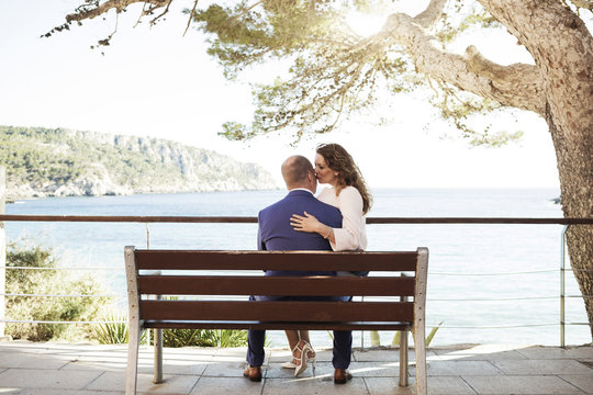 Spain, Majorca, woman kissing man on bench at the coast