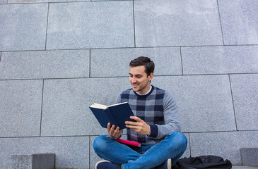 University.Smiling young student man holding and reading book in campus .Young smiling student outdoors Life style.City.Student.