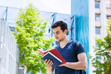 University.Smiling young student man holding and reading book in campus .Young smiling student outdoors Life style.City.Student.