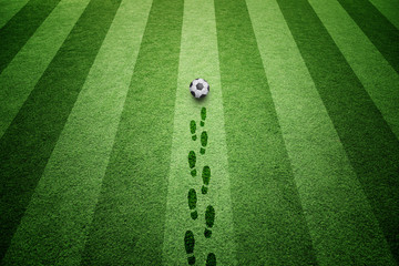 Socccer green grass field with soccer ball and shoe prints background. 