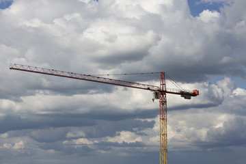 Tower crane. Big crane. Assembling of crane on dramatic cloudy background. Dangerous situation in height. Yellow crane with workman. High construction machinery with load, burden. Hook hangs on rope.