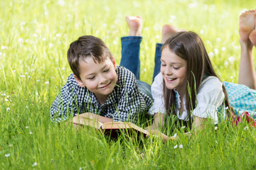 Zwei Kinder auf der Wiese liegend, haben Spaß beim Buch lesen