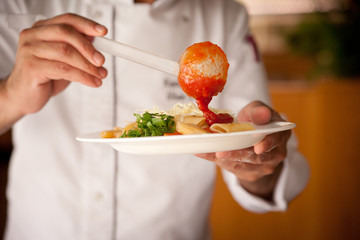 Chef preparing pasta with tomato sauce, cheese and herbs