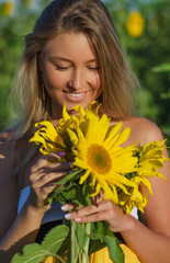 Portrait of a beautiful young blonde woman ion a background field of sunflowers