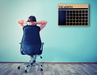 Woman sitting back on the office chair and looking at chalkboard calendar on wall background