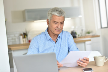 Fototapeta premium Smiling senior man at home using laptop