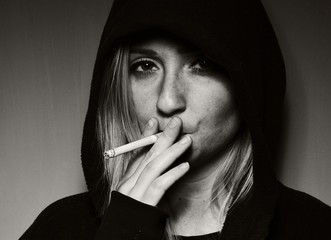 Rebellious teenager in a hooded sweatshirt smoking a cigarette.