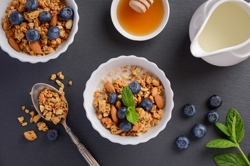Homemade granola with blueberries, milk and honey on black slate background, top view