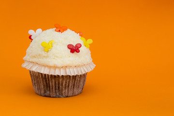 cupcake mit Kokosflocken und bunten Schmetterlingen dekoriert auf orangem Hintergrund
