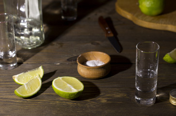 glass with tequila on a wooden table , green  ​​lime knife