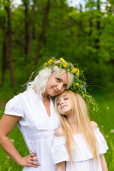 Beautiful and happy mum and daughter with wreaths on the head outdoors in the summer