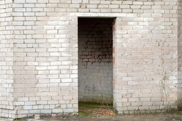 white cracked brick wall with a doorway of an abandoned house