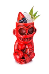 Red tiki mug in the form of monkey decorated with blueberry, strawberry, pineapple leaves and...