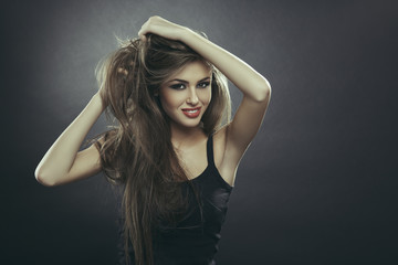 Beautiful sensual young lady posing with her hands through her long smooth healthy brown hair over dark grey background with copy space. Hair health, hair freshness, hair care.