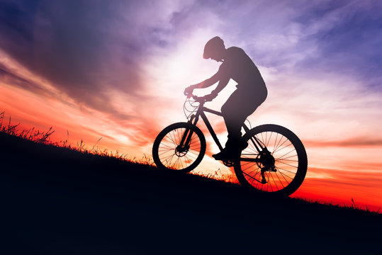 Silhouette of a biker on bike with sky background on sunset.