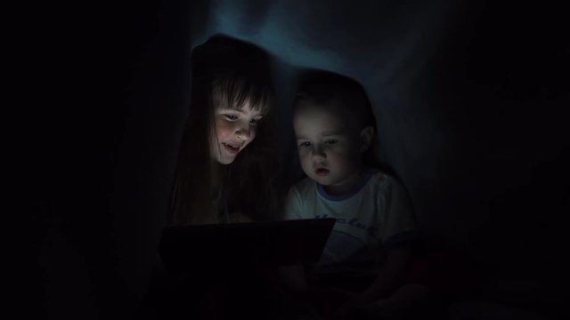 Girl and boy reading book under blanket