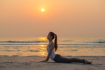 Fototapeta na wymiar Silhouette young woman practicing yoga on the beach at sunrise. 