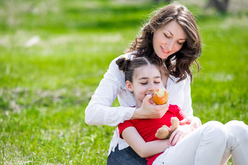 Mother and her child enjoy the early spring, eating apple, happy.