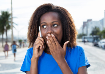 Afrikanische Frau im blauen Shirt überrascht am Telefon