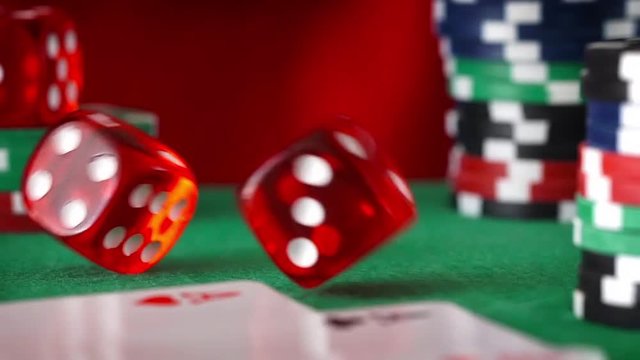 Red dice in sequence rolls, casino chips, cards on green felt