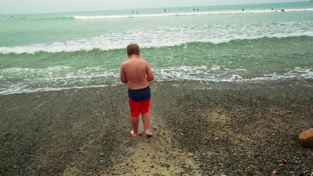 Slow motion of kid walking towards the ocean at the beach