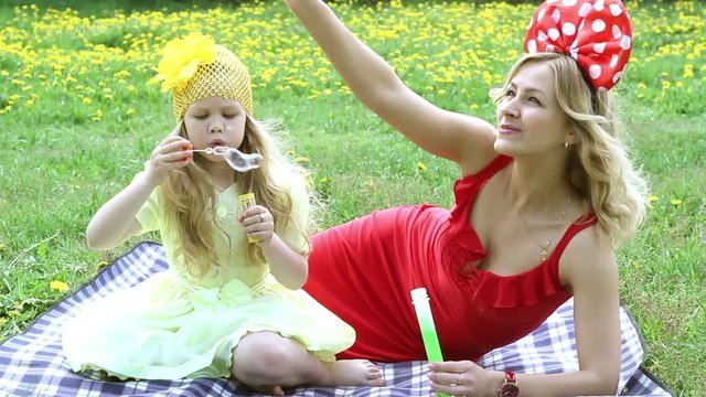 Beautiful woman and girl outdoors blowing bubbles, lying in the grass,smiling.