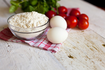 Cherry tomatoes, eggs, flour and basil on the table