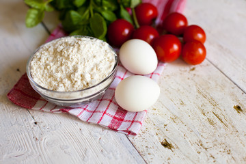 Cherry tomatoes, eggs, flour and basil on the table