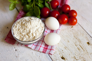 Cherry tomatoes, eggs, flour and basil on the table