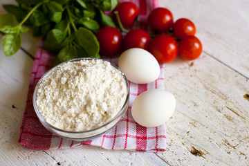 Cherry tomatoes, eggs, flour and basil on the table