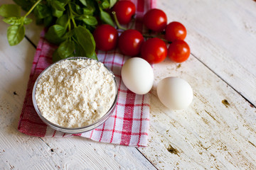 Cherry tomatoes, eggs, flour and basil on the table