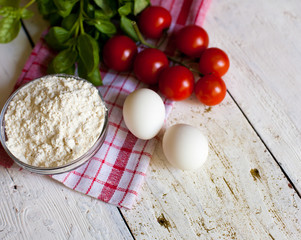 Cherry tomatoes, eggs, flour and basil on the table
