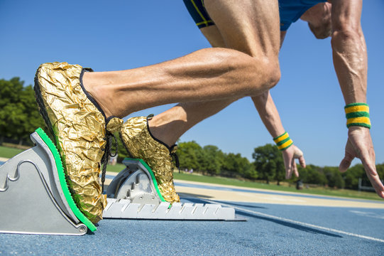 Athlete in gold shoes starting a race from the starting blocks on a blue running track 