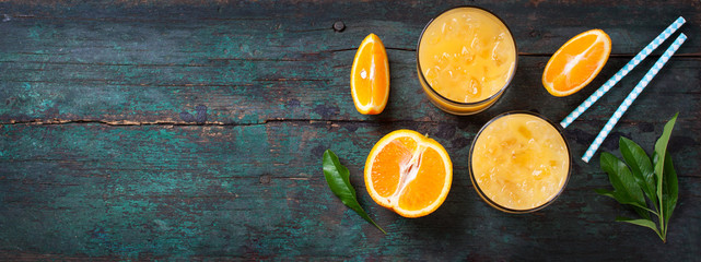 Fresh orange juice with crushed ice and fresh oranges and blue straws on an old vintage exotic background with copy space, top view