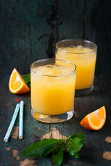 Fresh orange juice with crushed ice and fresh oranges and blue straws on an old vintage exotic background, closeup