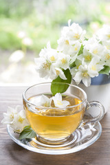 Transparent glass cup of tea with jasmine and blooming jasmine branch in blue ceramic cup on wooden table