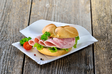 Garniertes Brötchen mit Schinkenwurst auf Pappteller mit Serviette - Roll with sliced ham sausage...