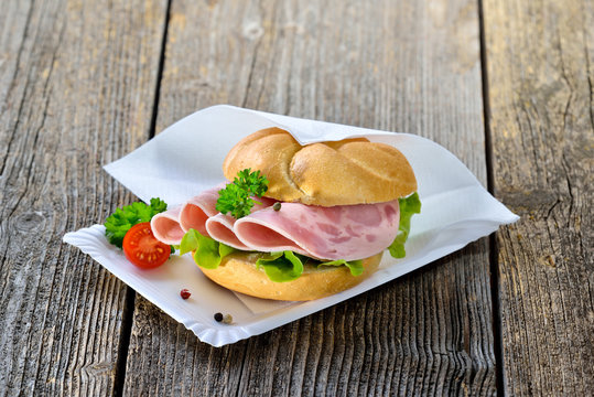 Garniertes Brötchen mit Schinkenwurst auf Pappteller mit Serviette - Roll with sliced ham sausage on a paper plate wth a napkin