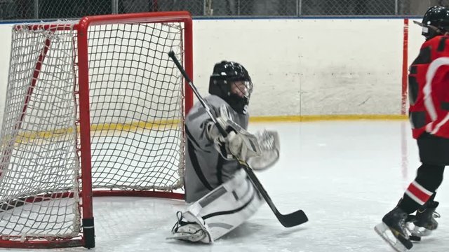 Kids playing hockey on ice rink: little goaltender trying to prevent scoring the goal, falling and trying to stand up