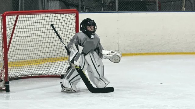 Little boy goaltender practicing hockey skills on the ice rink; he trying to catch the puck but losing it