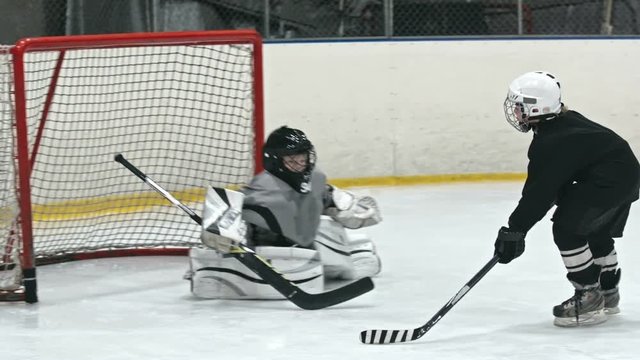 Little kids training professional hockey on an ice rink: one boy heading puck into the net and scoring goal