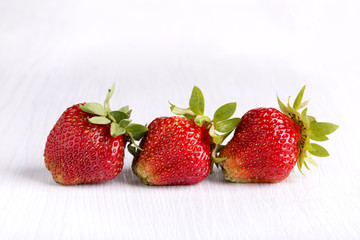 Three ripe red strawberries on white wooden blackboard
