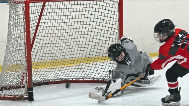 Kids playing professional hockey on ice rink: boy shooting the puck and goalie losing his stick and falling down