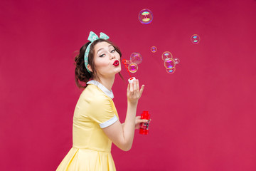 Obraz na płótnie Canvas Playful cute pinup girl in yellow dress blowing soap bubbles