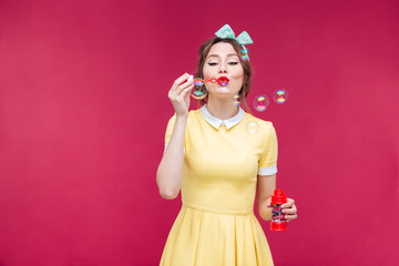 Attractive pinup girl in yellow dress blowing soap bubbles