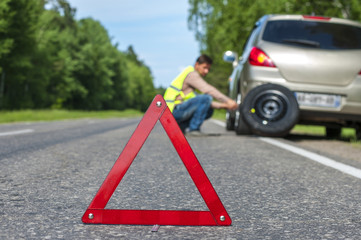 Red triangle warning sign and man changing the tire