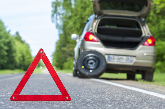 Red warning sign and broken car on the roadside