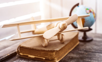 Fototapeta na wymiar beautiful handmade wooden toy-plane on a book with globe on the background